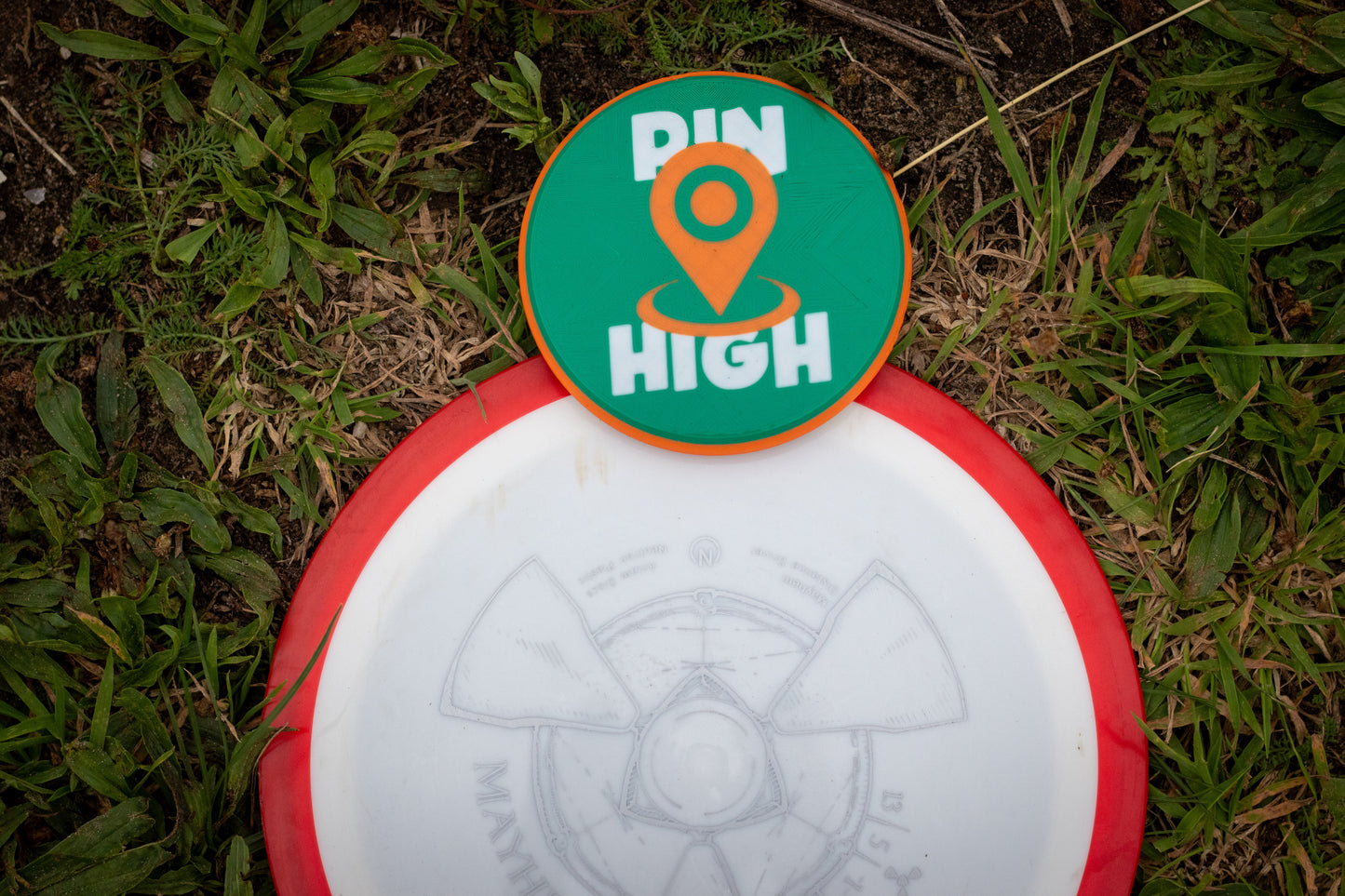 Disc golf disc with 'Pin High' disc golf mini marker on grass