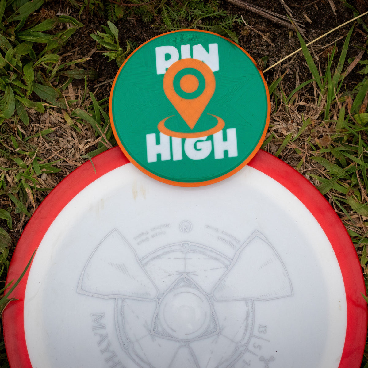 Disc golf disc with 'Pin High' disc golf mini marker on grass